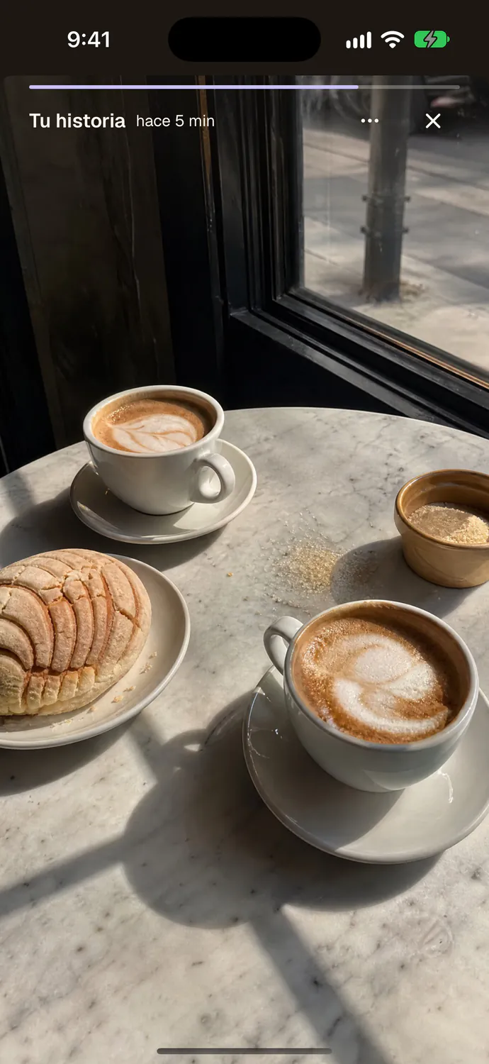 Your story: two coffees and a concha on a marble table by the window.